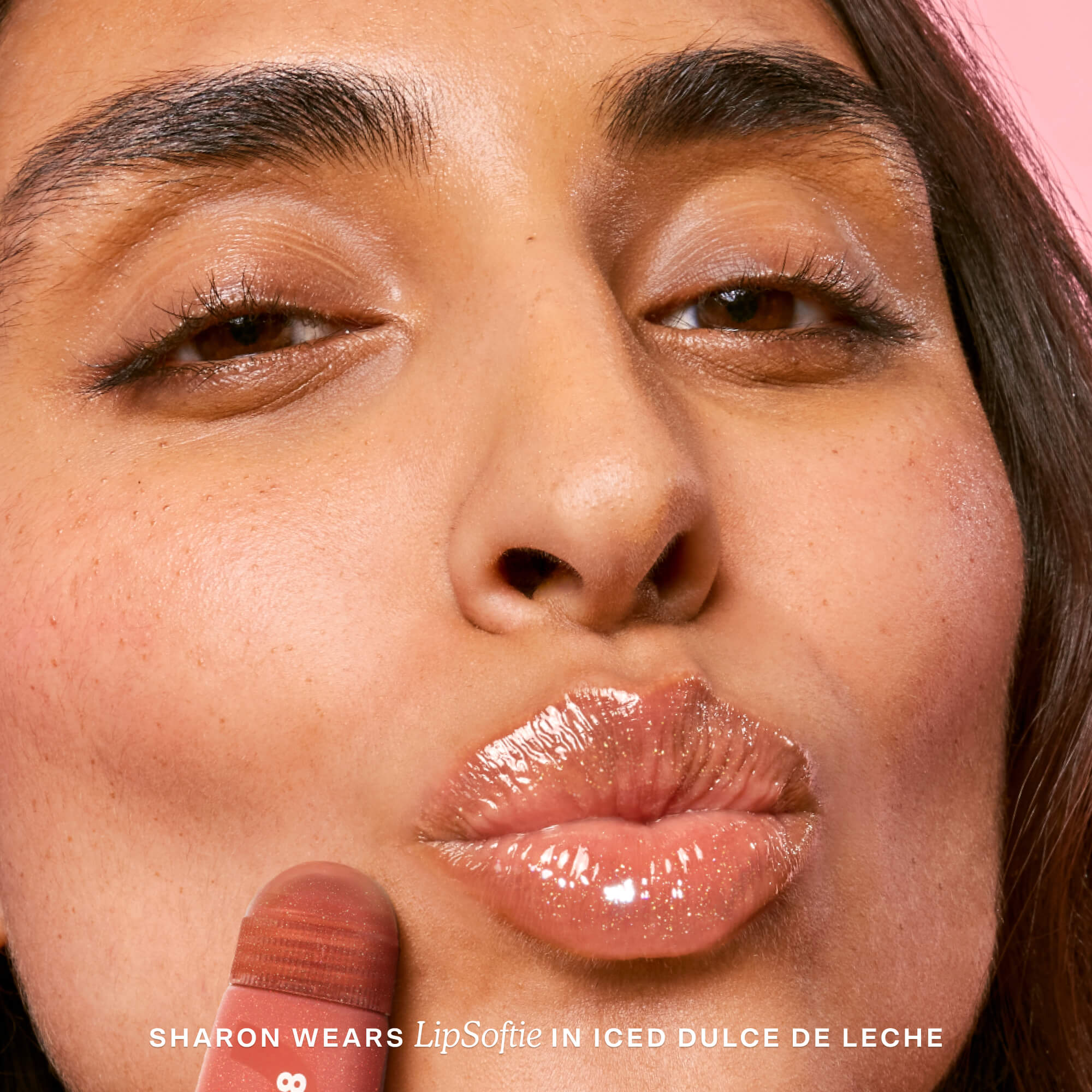 Close-up of a person wearing lip gloss with text indicating product name and color. [Iced Dulce de Leche]