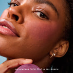 A person holds Tower 28 Beauty’s GetSet Powder Blush in the shade Pali Punch with a swatch of lavender pigment on their cheek. [Pali Punch]