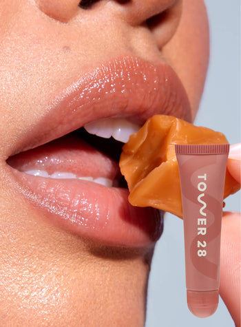 [A close up of a model wearing Tower 28 Beauty's LipSoftie™ Lip Treatment in Dulce de Leche on her lips]